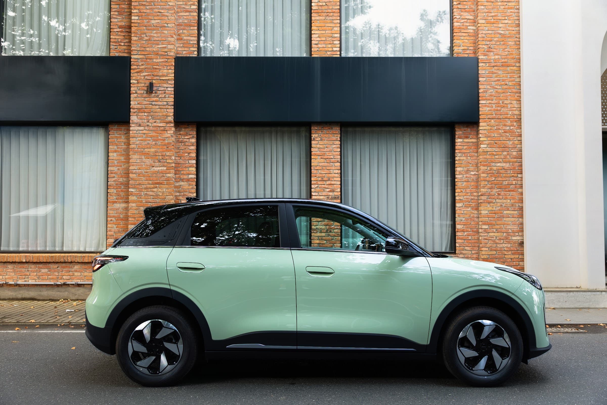 Geely E2 in Mintgrün von der Seite vor einer Backsteinfassade